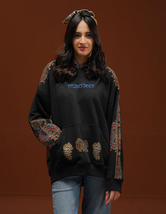Woman wearing a black hoodie with colorful patterns on the sleeves against a brown background