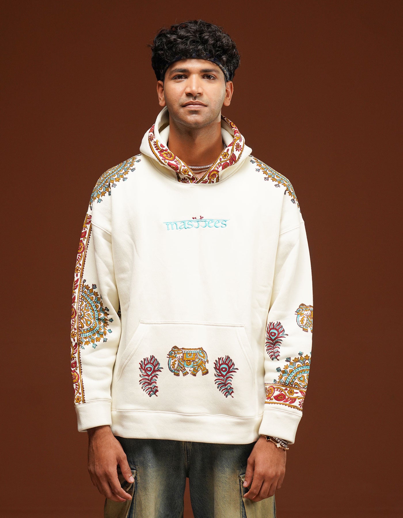 Man wearing a white hoodie with colorful embroidery on a brown background