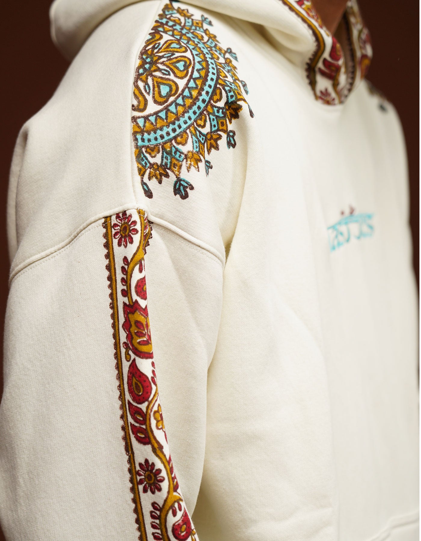 Close-up of a white hoodie with colorful embroidery on the sleeves and chest.