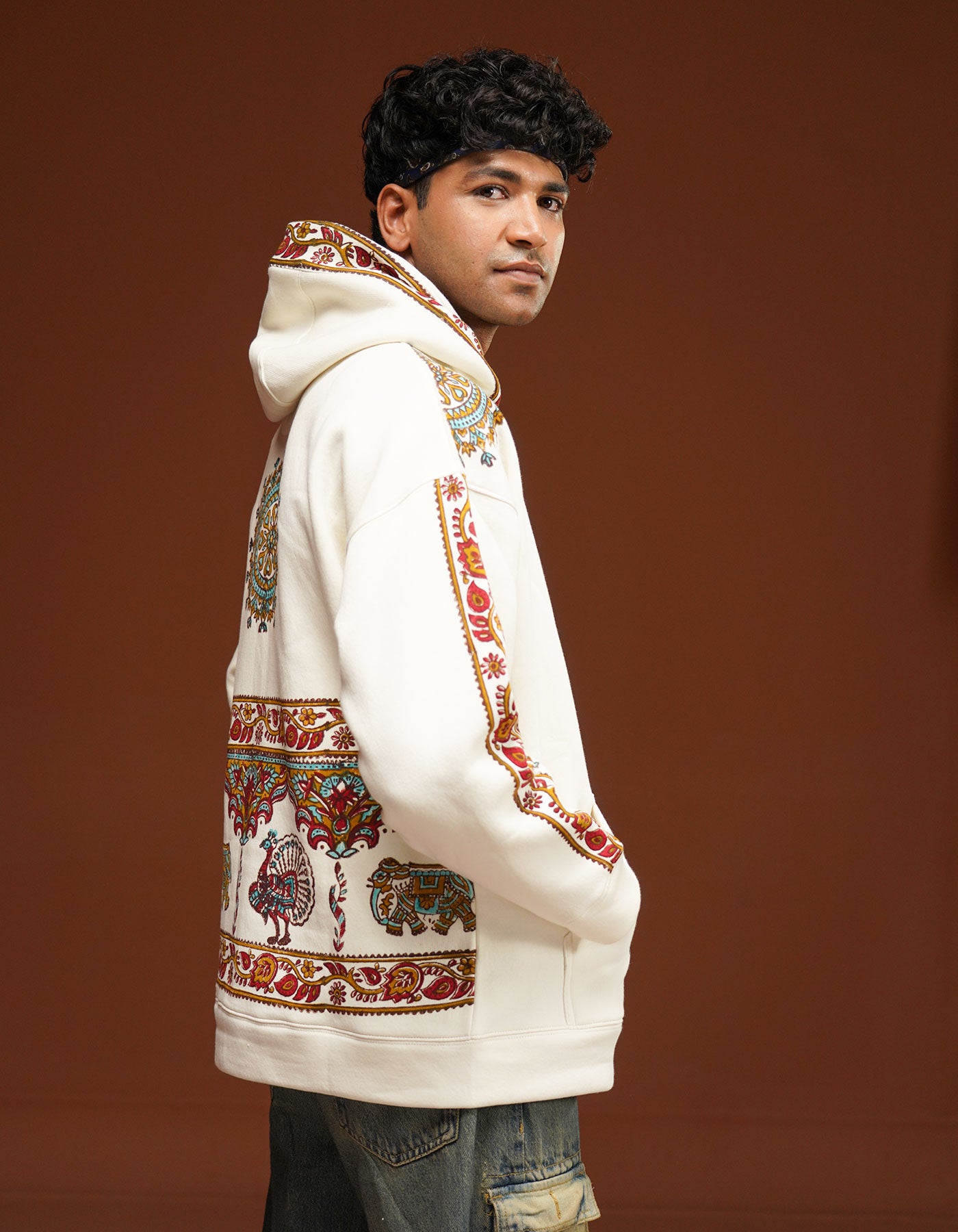 Person wearing a white hoodie with colorful patterns on a brown background