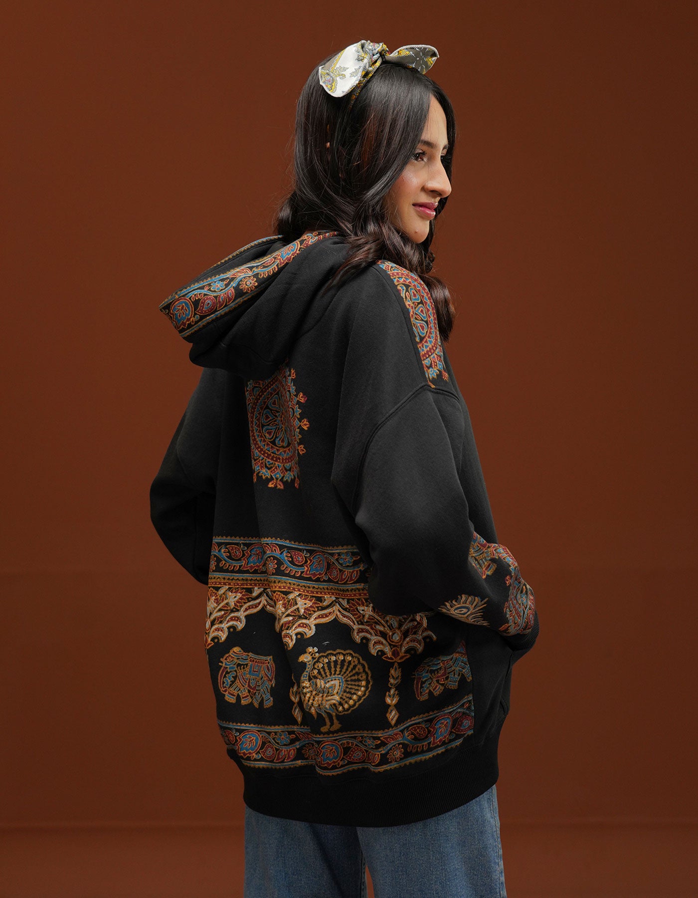 Woman wearing a black hoodie with intricate patterns on a brown background