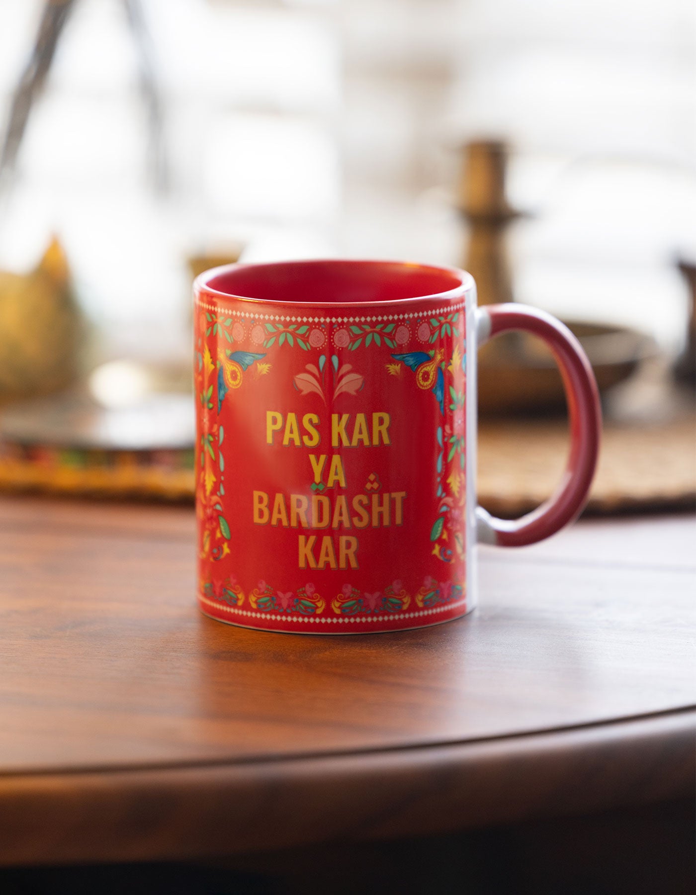 Red mug with floral patterns and text on a wooden surface