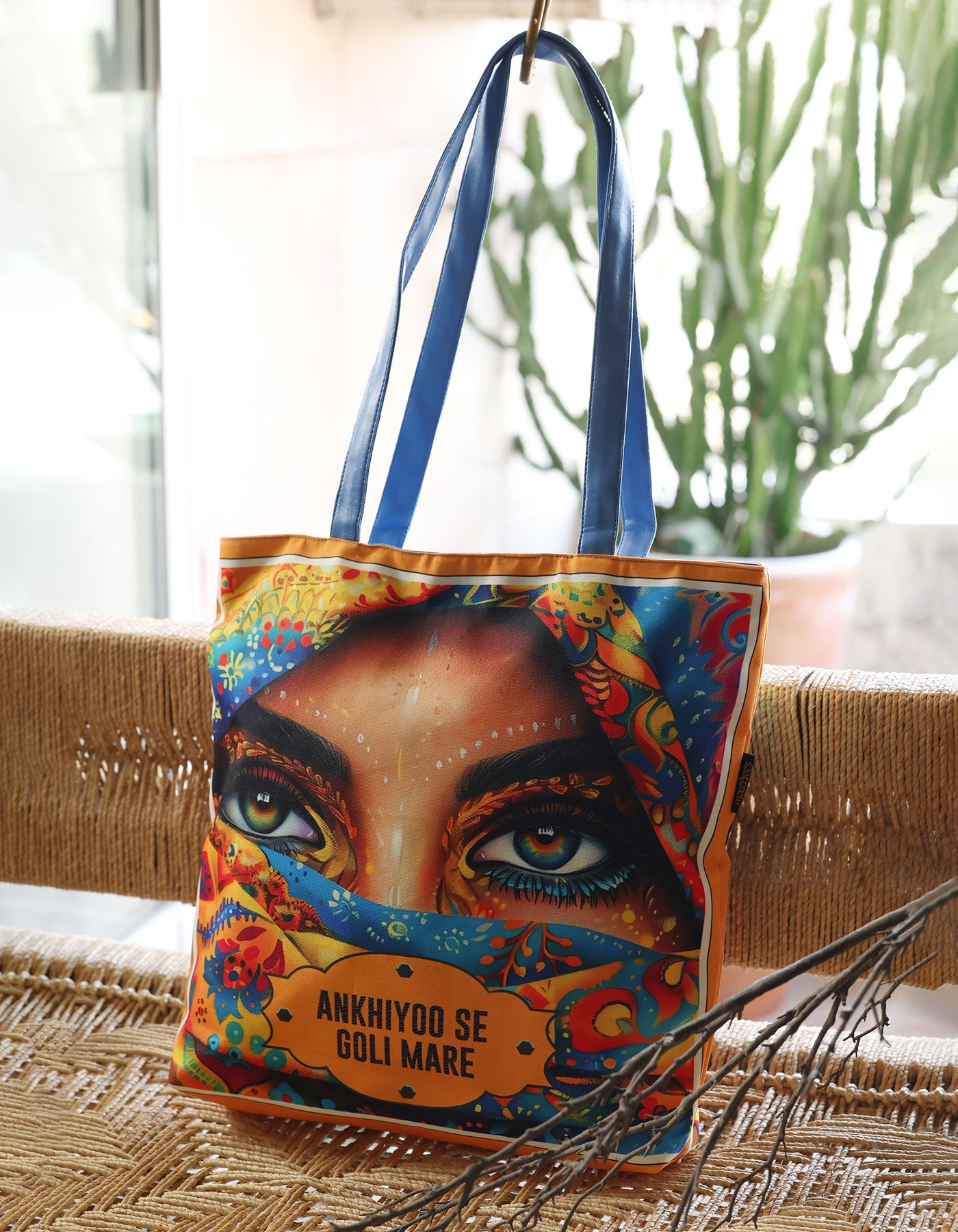Tote bag with a colorful design of a face and text, placed on a woven surface.