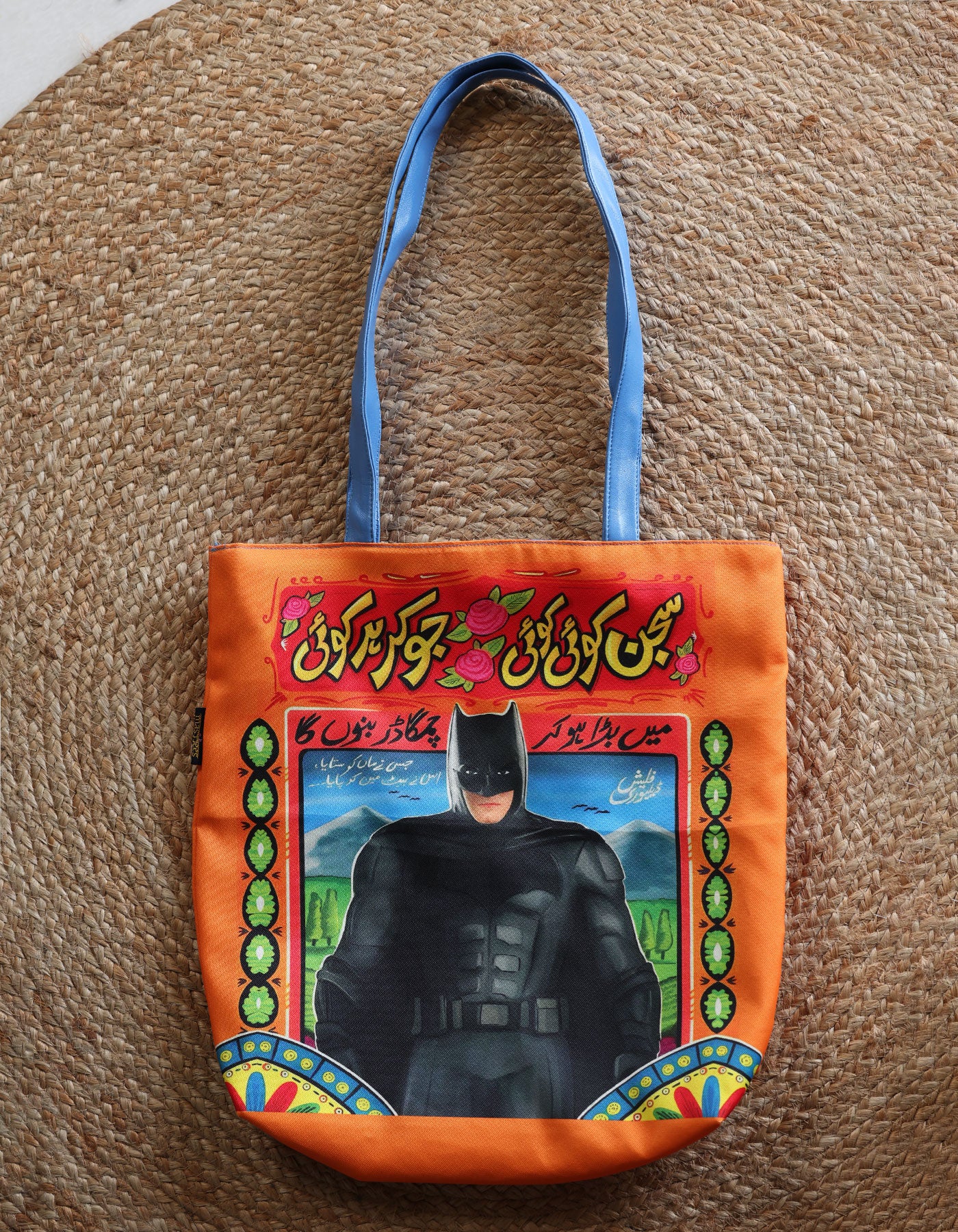 Tote bag with Batman design on an orange background, placed on a textured surface.