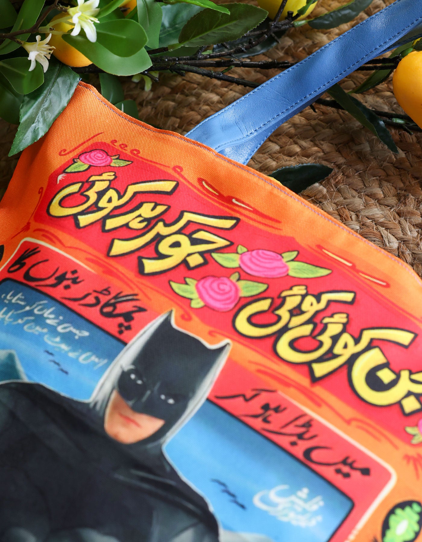 Colorful bag with text and a cat mask on a textured surface with greenery.