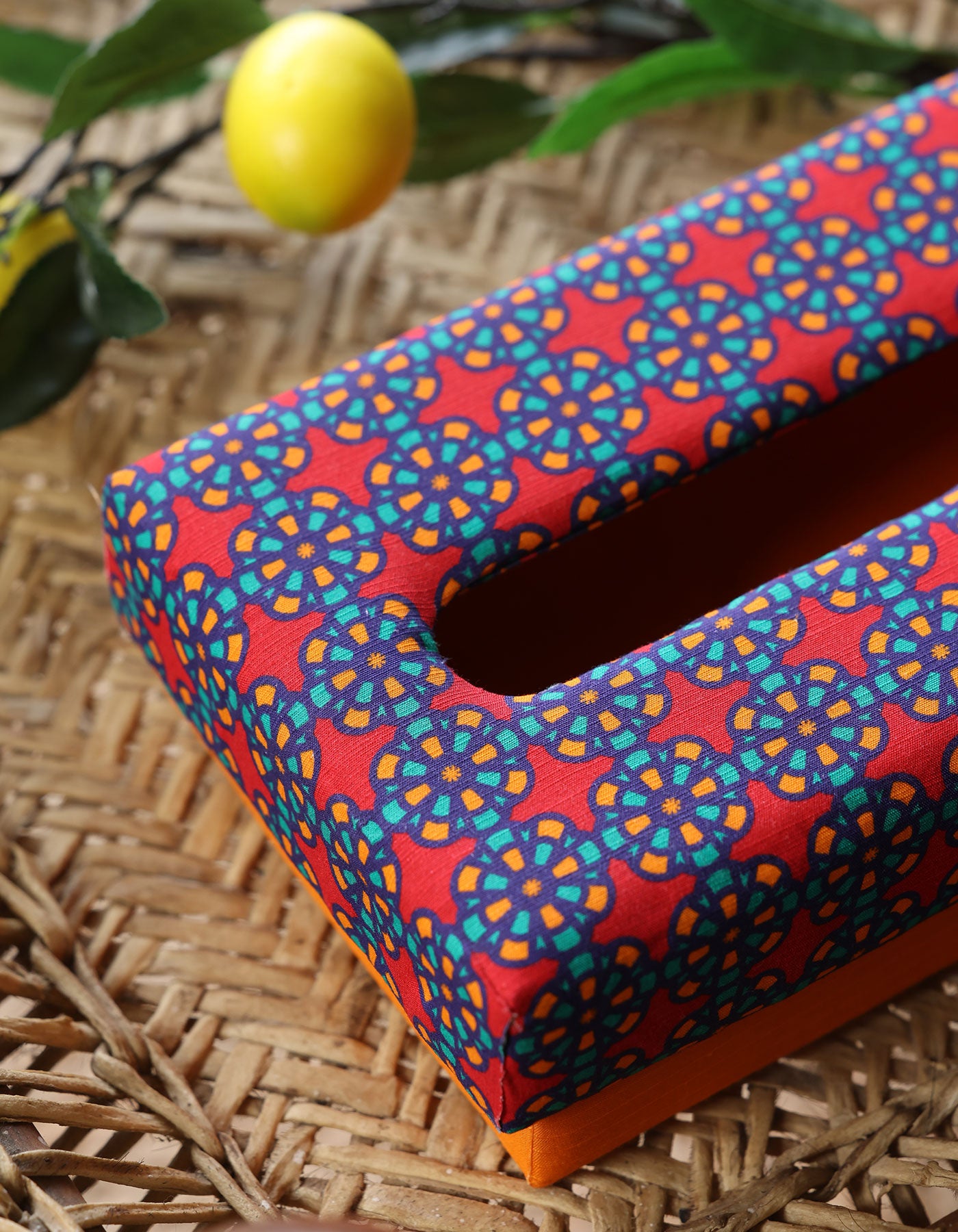 Colorful patterned tissue box on a woven surface with a lemon in the background