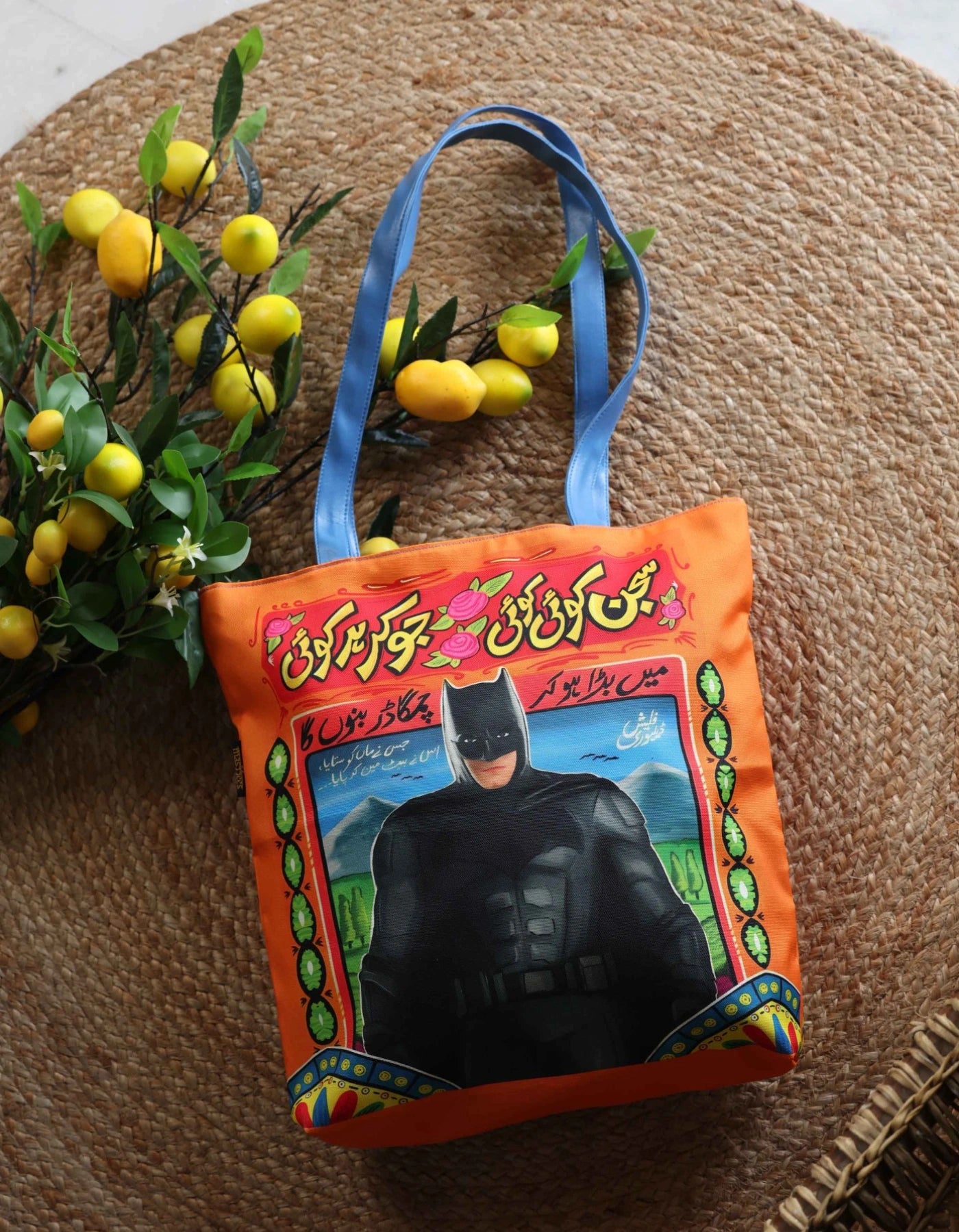 Handbag with Batman design on an orange background, surrounded by lemons and greenery.