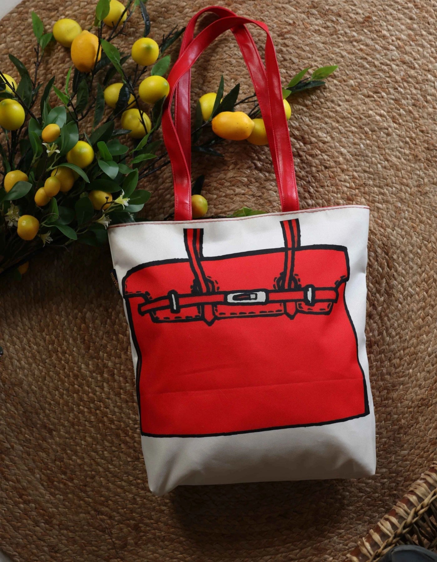 White tote bag with red handle and black design on a textured surface with decorative elements.