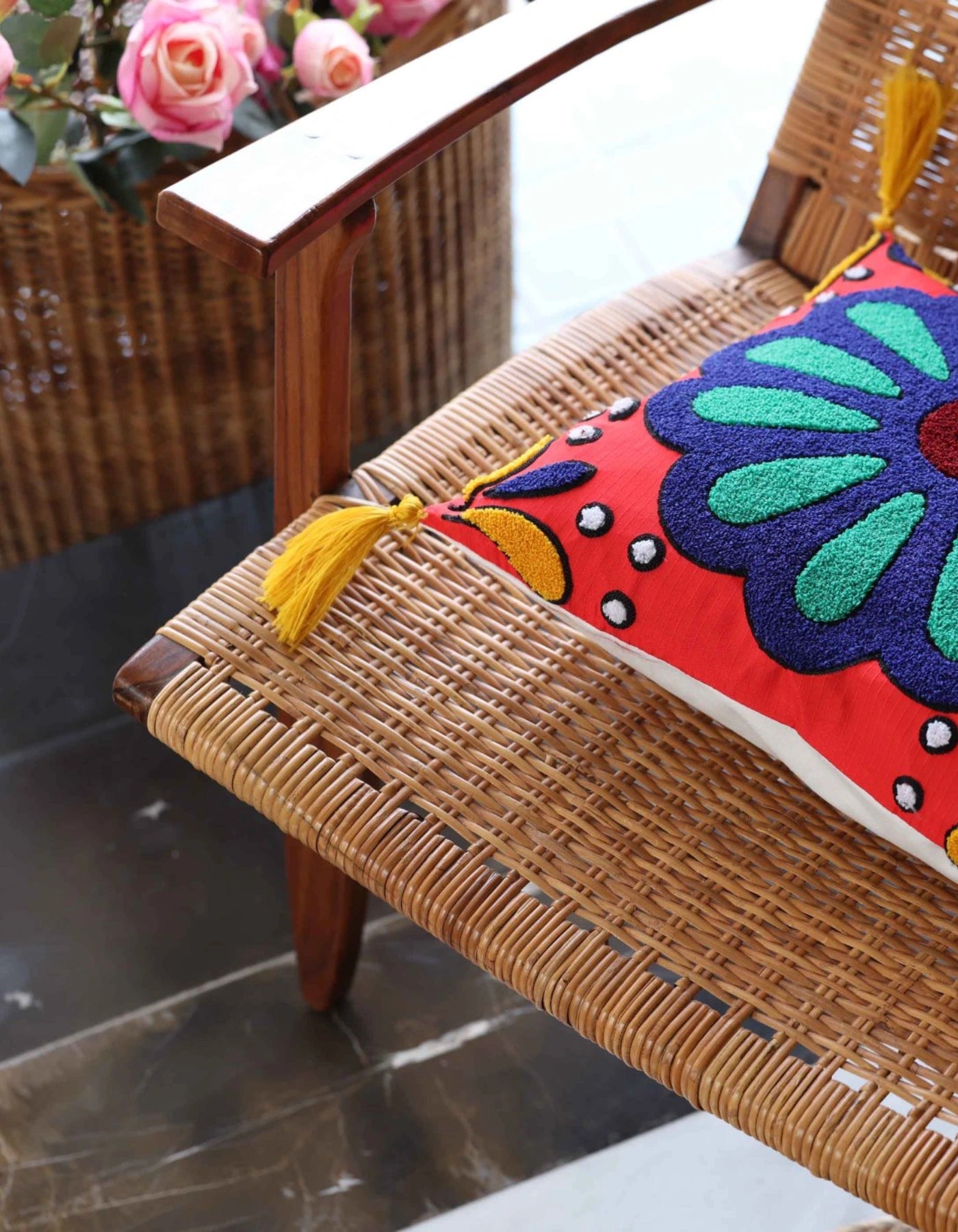 Colorful embroidered pillow on a wicker chair with flowers in the background