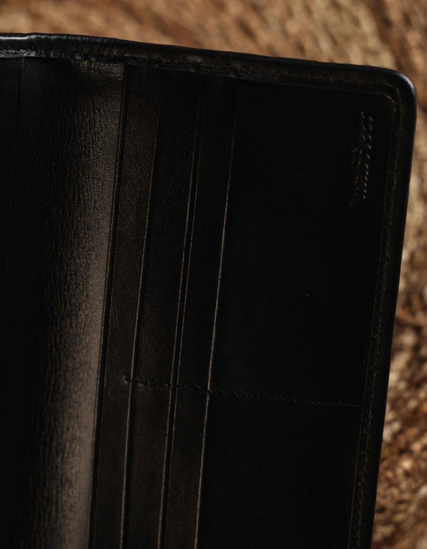 Close-up of a black leather wallet with stitching details on a textured brown background