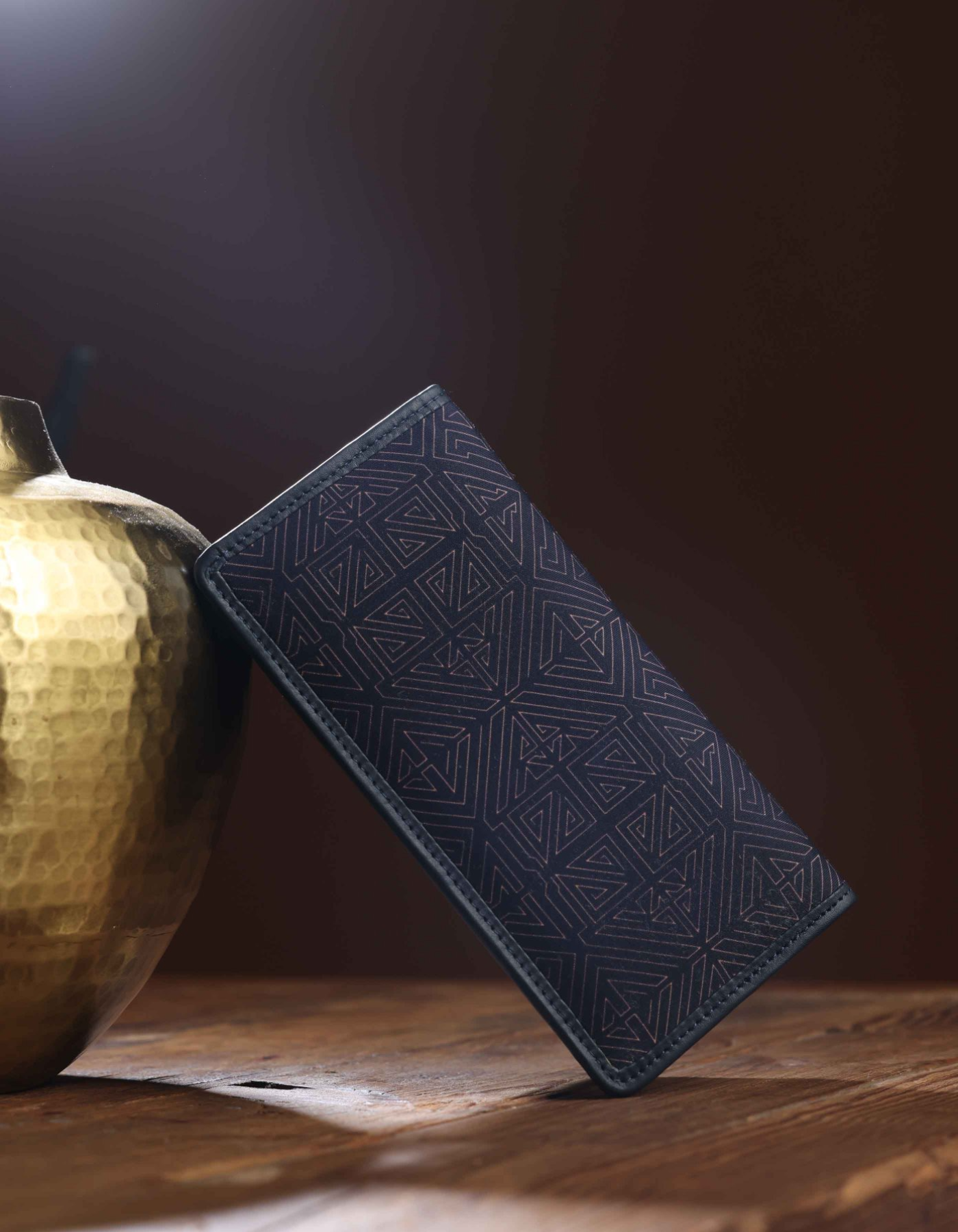 Dark blue textured wallet on a wooden surface with a gold vase in the background