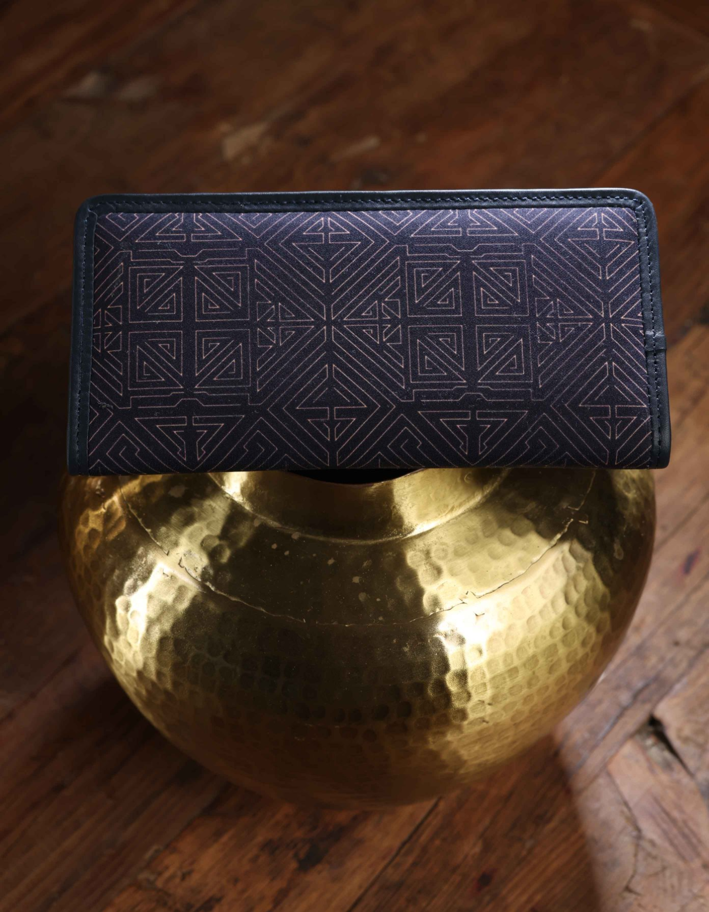 Black wallet with geometric pattern on a gold spherical object on a wooden surface