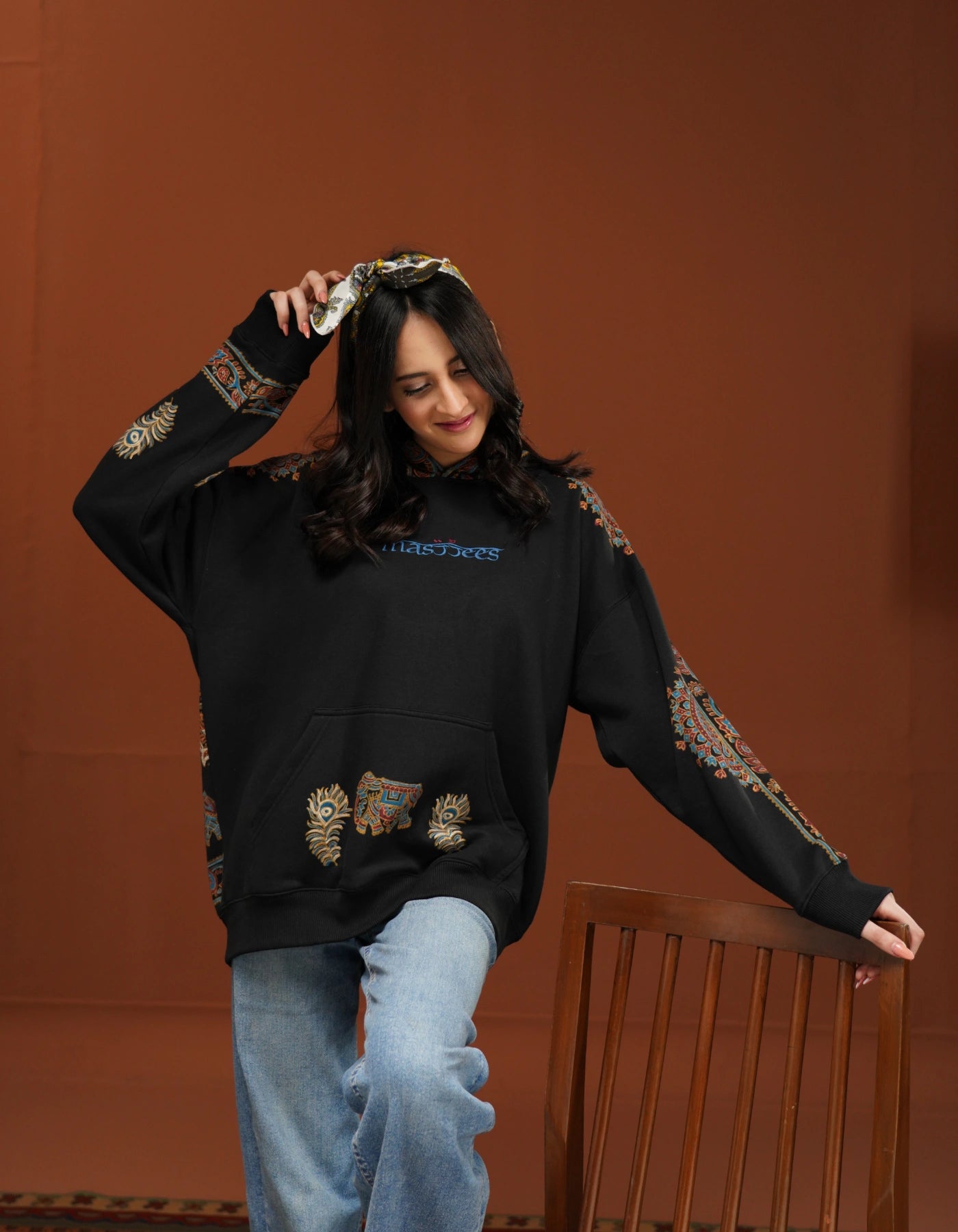 Person wearing a black hoodie with decorative elements on a brown background