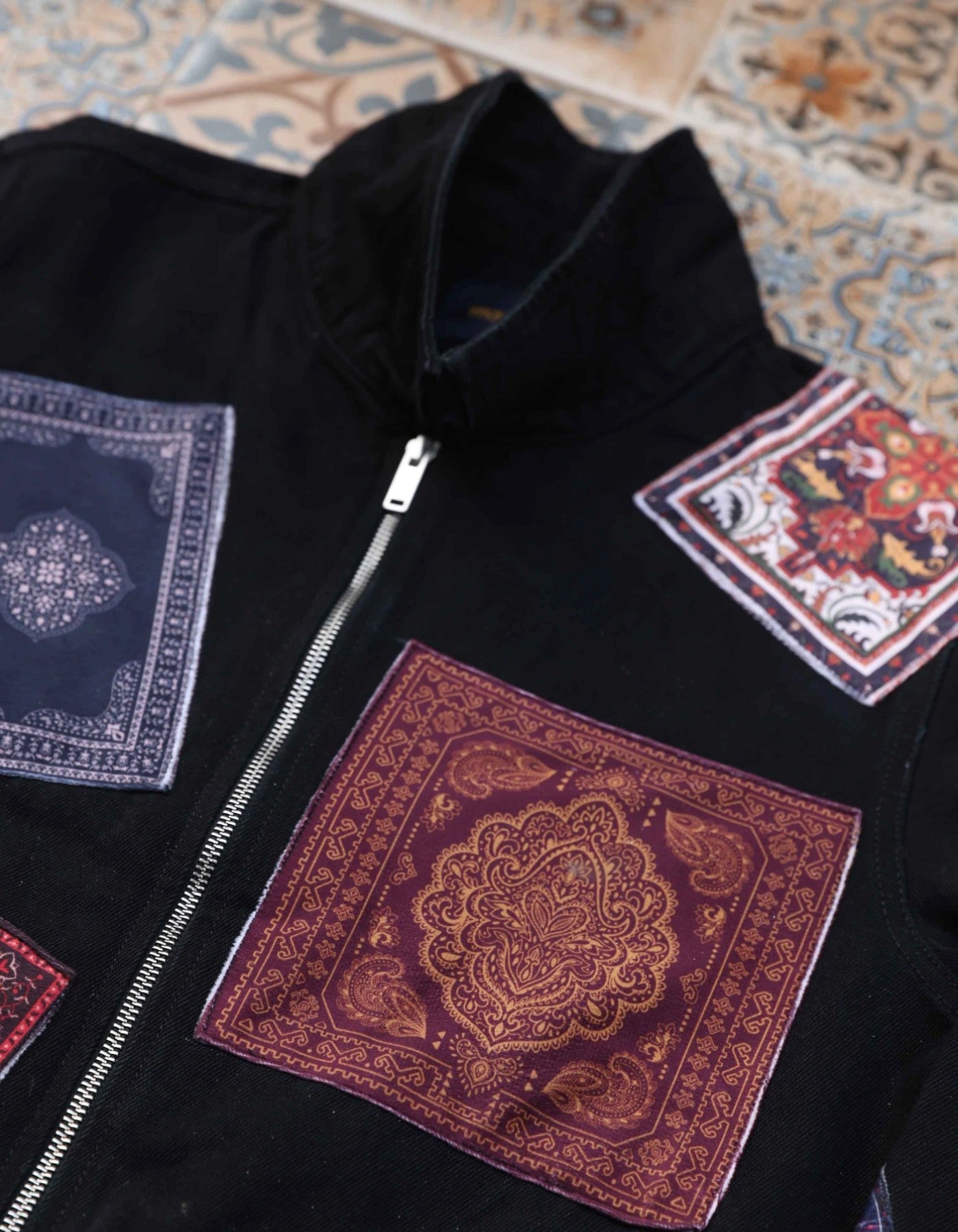 Black jacket with colorful patch designs on a patterned fabric background